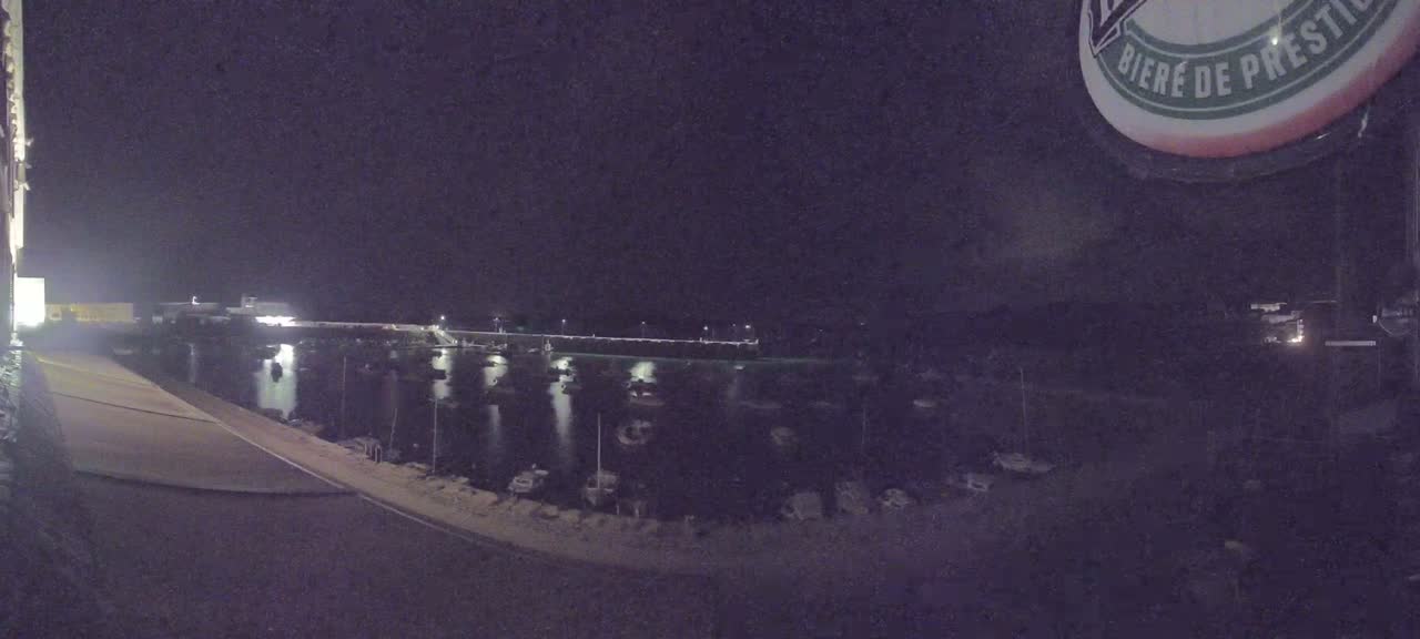 A nighttime view of a harbor filled with boats, illuminated by lights along a seawall.