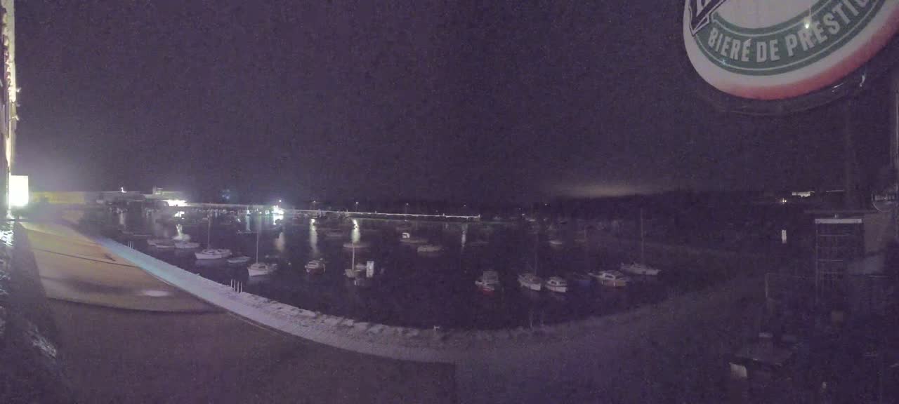 A nighttime view of a calm harbor filled with numerous small boats, under a dark sky.