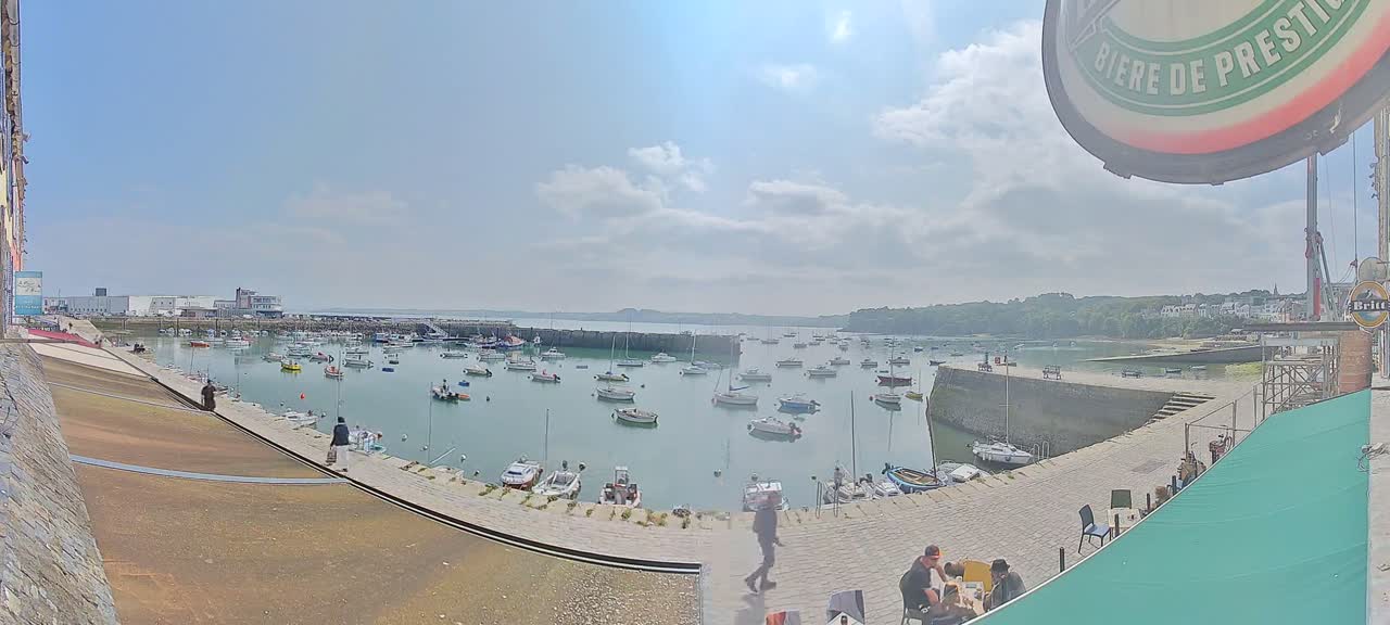 A harbor filled with numerous boats is viewed from a waterfront patio on a partly sunny day.