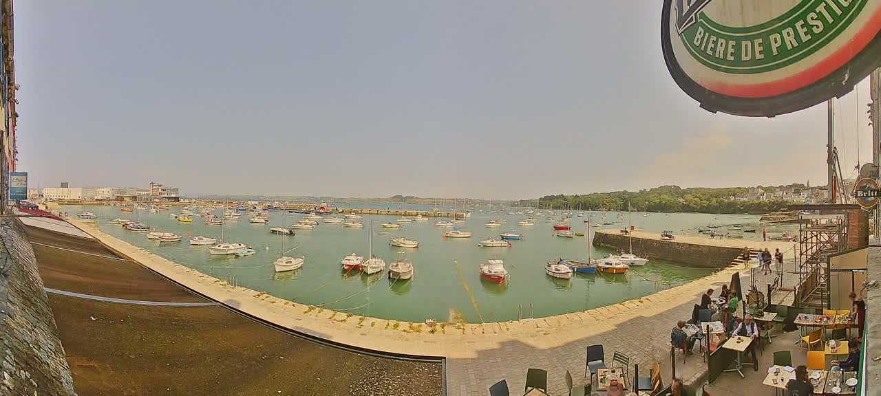 A harbor filled with numerous small boats is viewed from an outdoor cafe on a sunny day.