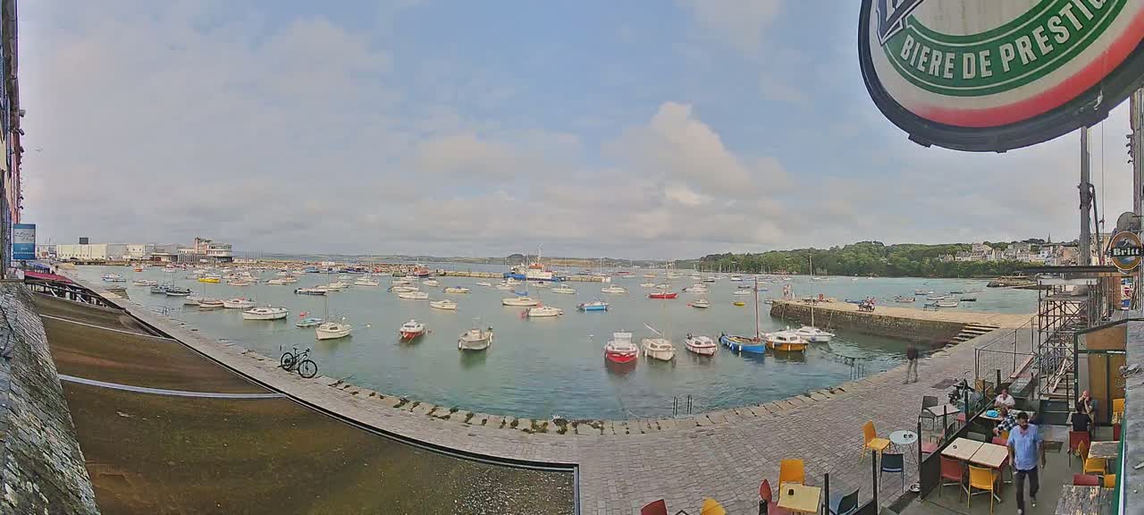 A harbor filled with numerous small boats under a partly cloudy sky, viewed from a waterfront patio with a bicycle nearby.