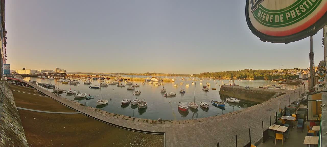 A harbor filled with numerous small boats sits under a clear, pale-orange sunset sky.
