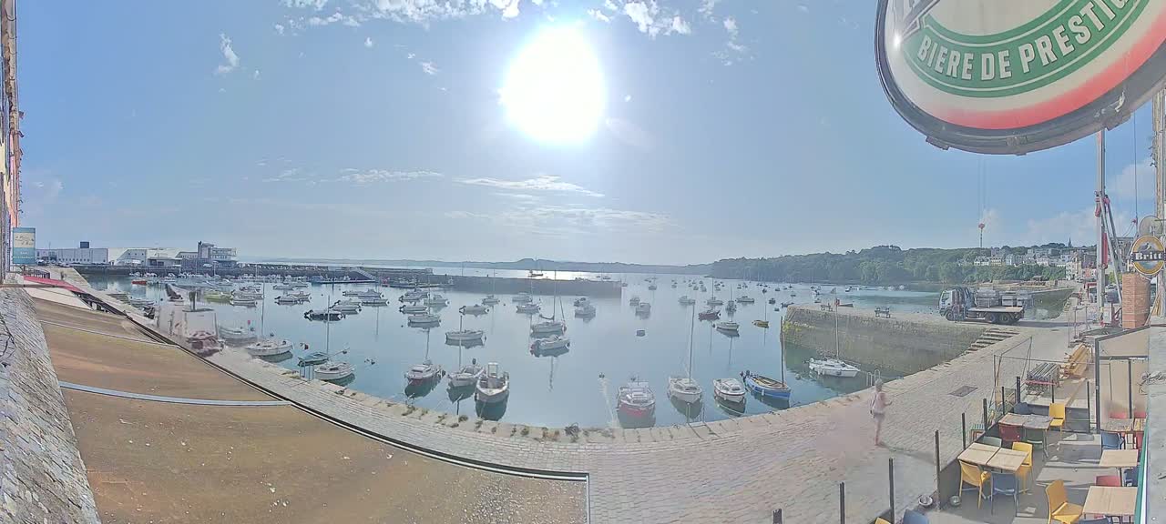 A sunny harbor filled with numerous sailboats and motorboats, under a bright, mostly clear sky.