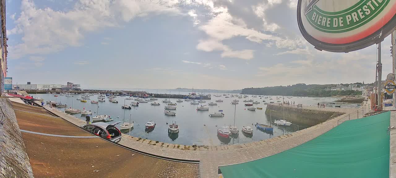 A harbor filled with numerous sailboats and motorboats under a partly cloudy sky.