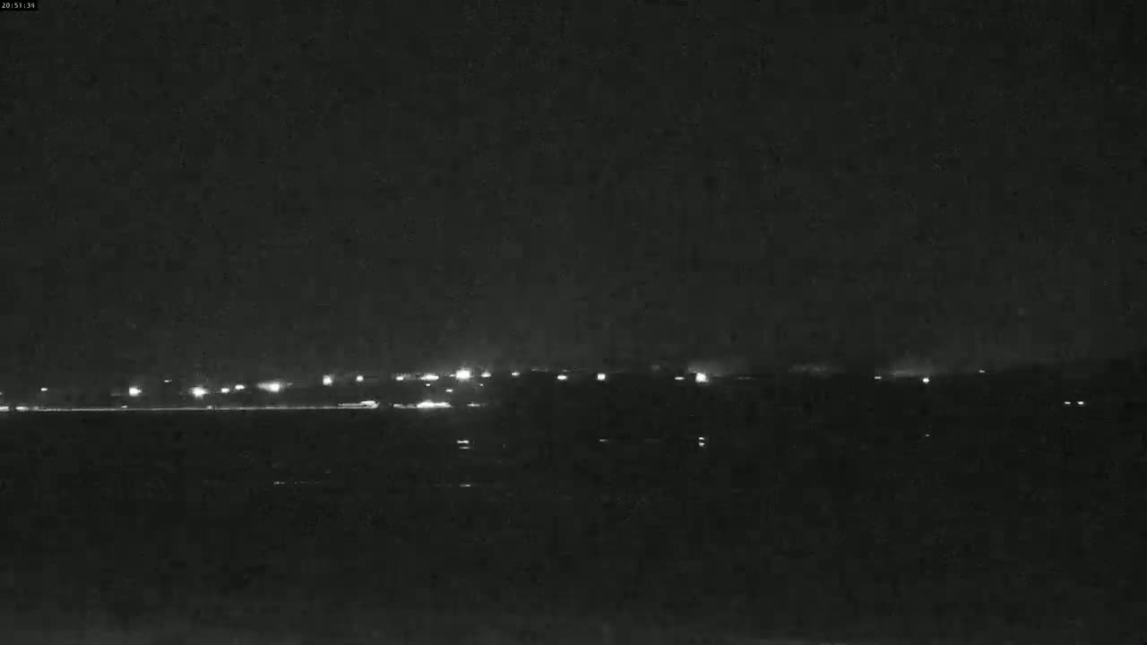 A nighttime view shows a line of distant lights on a dark horizon under a clear, black sky.