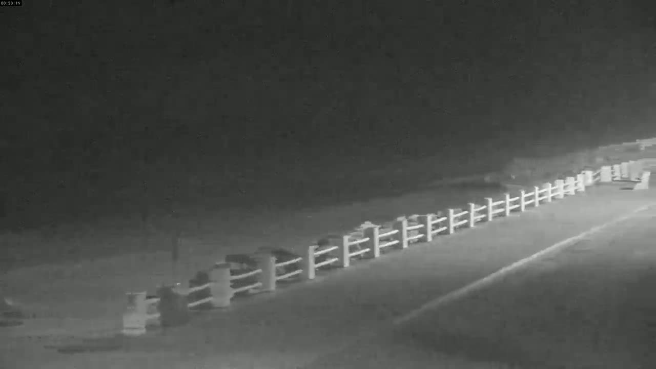 A long white fence runs alongside a dark road at night.