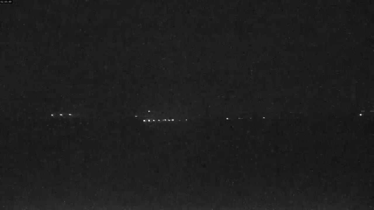 A dark, nighttime scene shows a line of distant lights at the horizon.