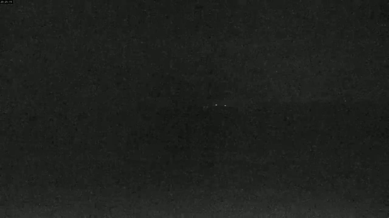 A dark, possibly nighttime, outdoor scene shows a mostly clear sky with two faint, distant lights.