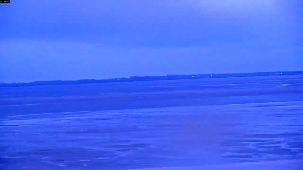 A flat, wide expanse of land or shallow water stretches to a dark horizon under a twilight-blue sky.