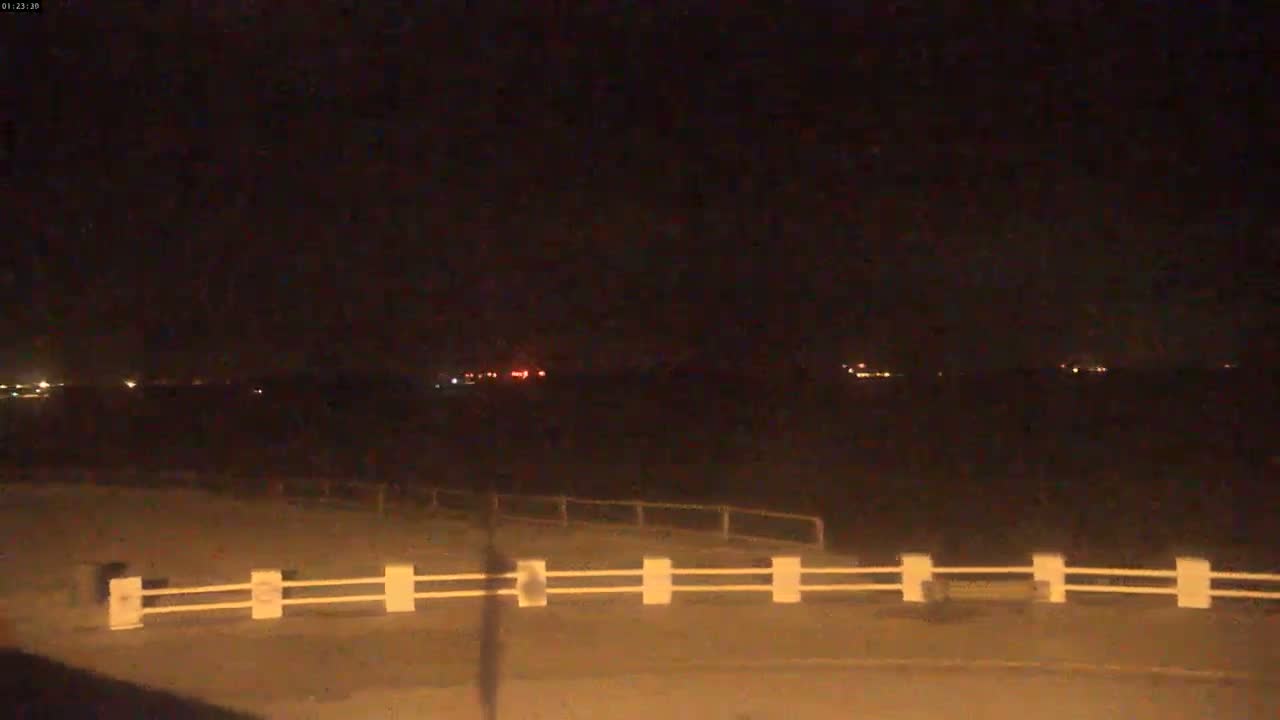 A nighttime view shows a low white railing in the foreground, with distant lights visible across a dark expanse under a clear, dark sky.