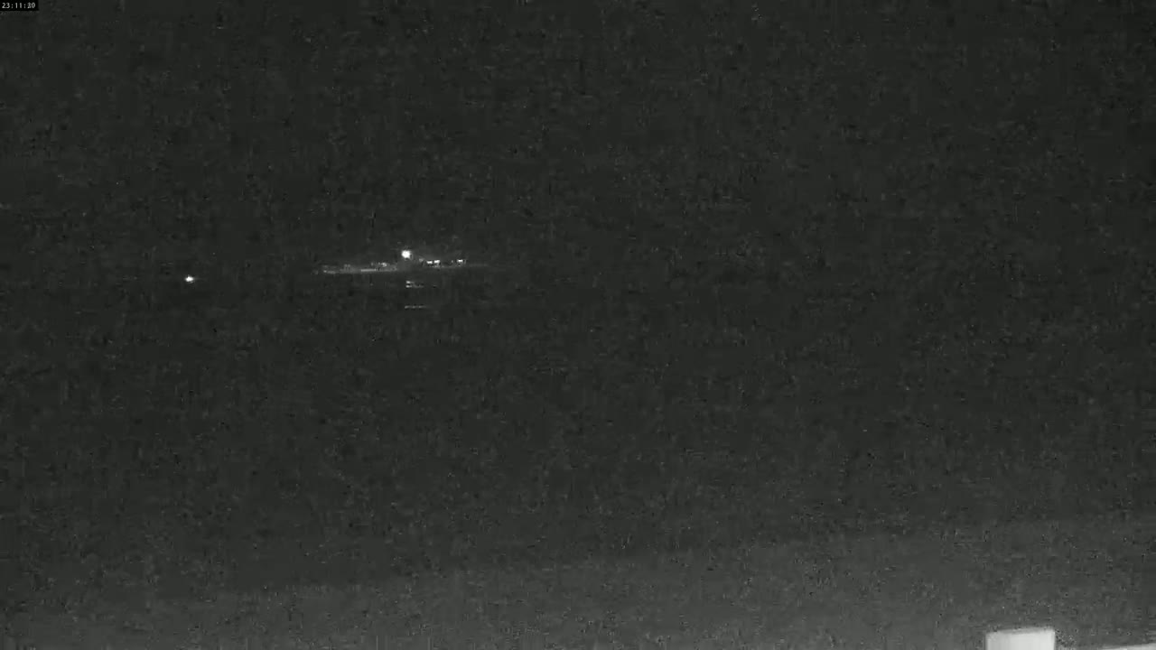 A nighttime, low-light image shows a dimly lit horizon with a few faint lights in the distance.
