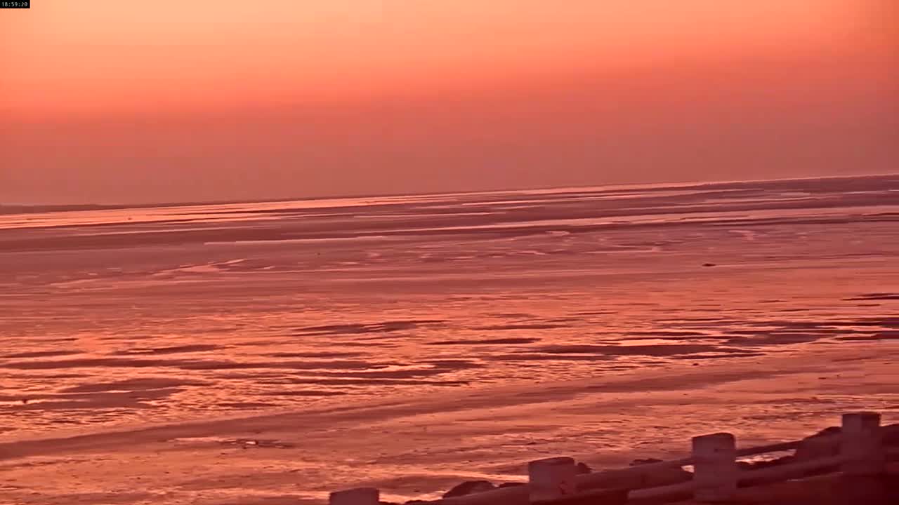 A wide expanse of reddish-hued tidal flats stretches to a similarly colored horizon under an orange sunset sky.