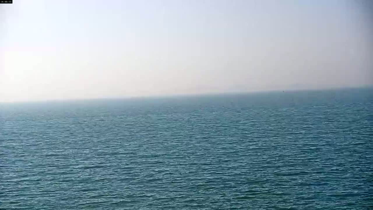 A hazy, calm ocean stretches to the horizon under a bright, pale sky.