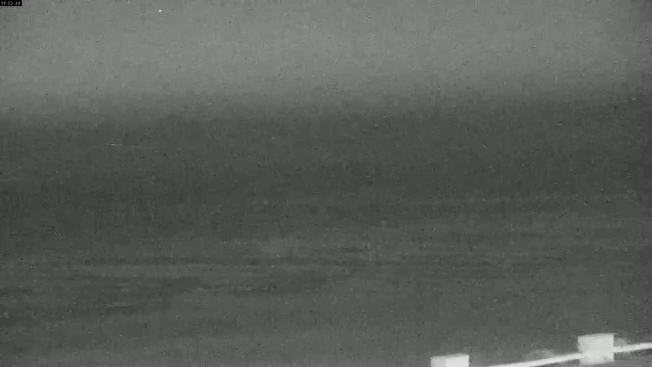 A nighttime, low-light image shows a dark, possibly snowy or rainy, landscape with a blurry horizon and indistinct features in the foreground.