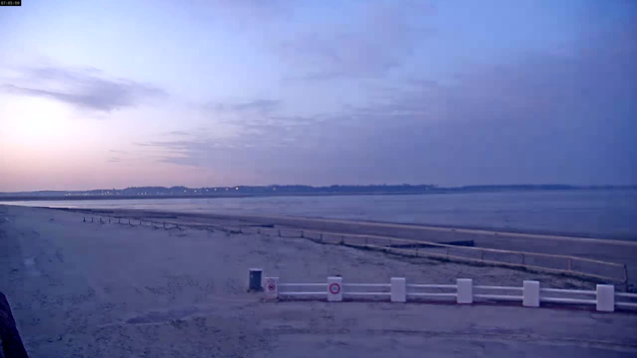 A sandy beach stretches towards a calm body of water under a pale, twilight sky.