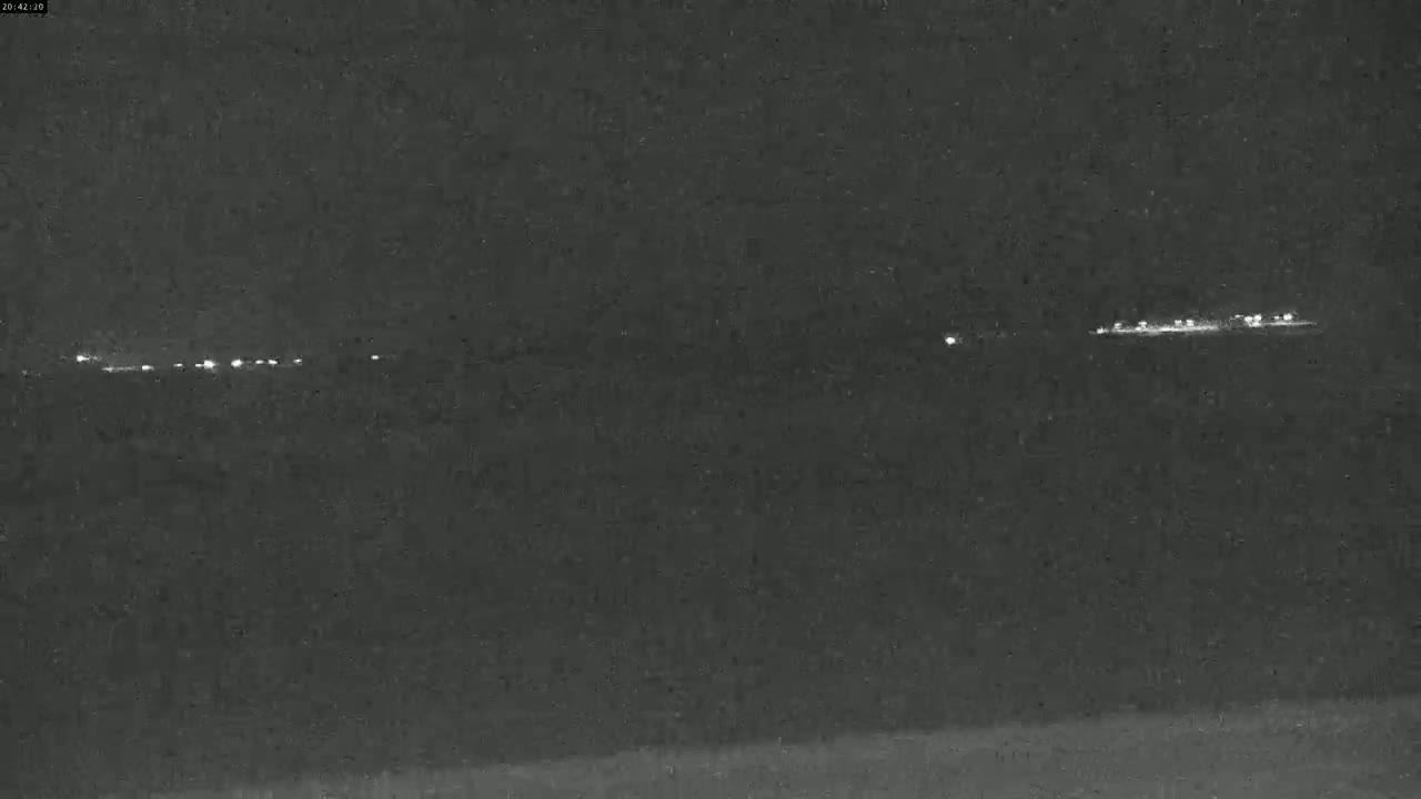 A line of distant lights is visible at night across a dark, seemingly flat landscape.