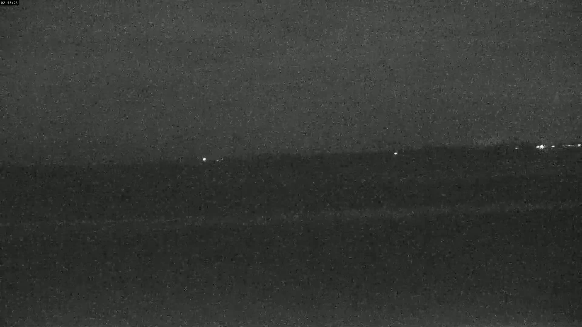 A dark, nighttime image shows a flat horizon line with a few faint lights visible in the distance.