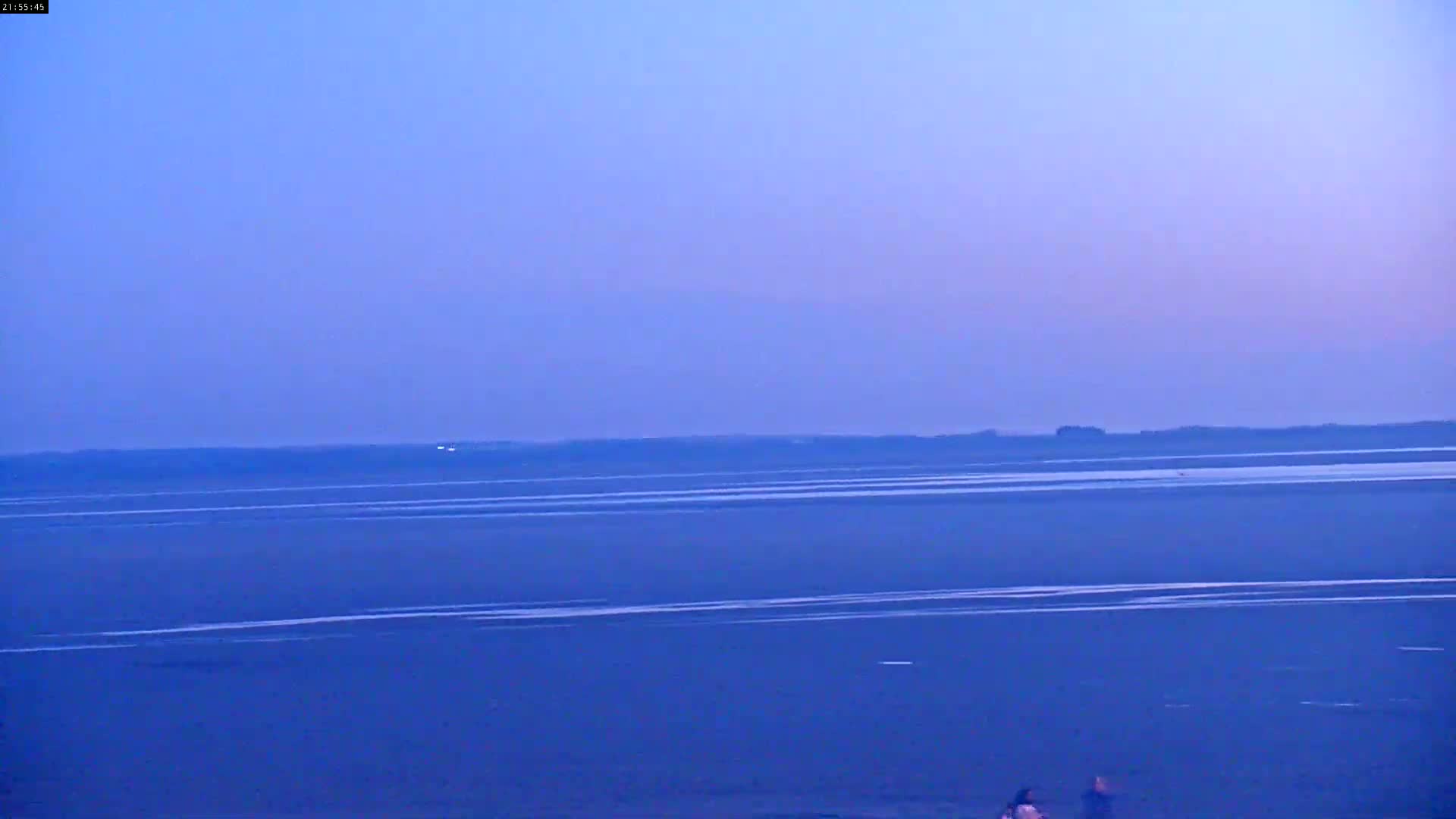 A calm, twilight-blue body of water stretches to a dark horizon line under a clear, dusky sky.