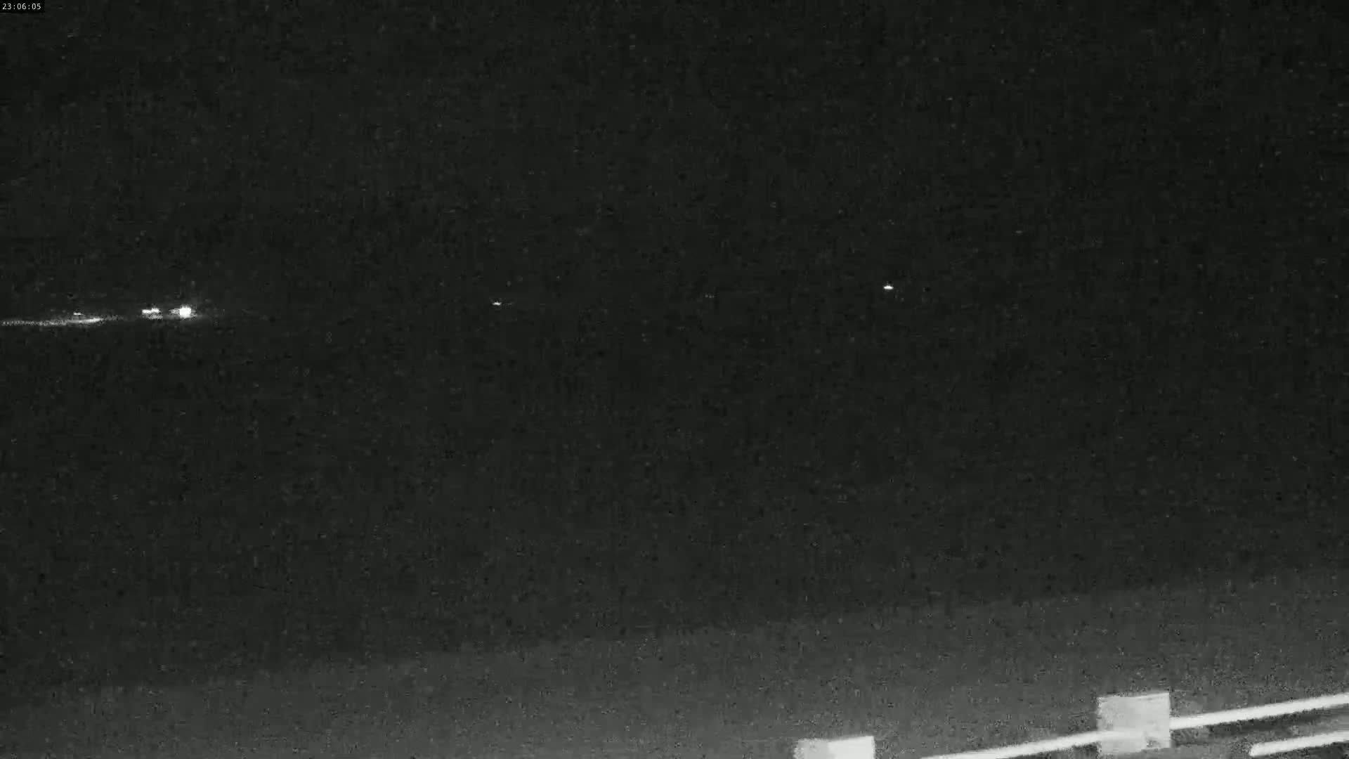 At night, several distant lights are visible over a dark, flat expanse of land with a low barrier in the foreground.