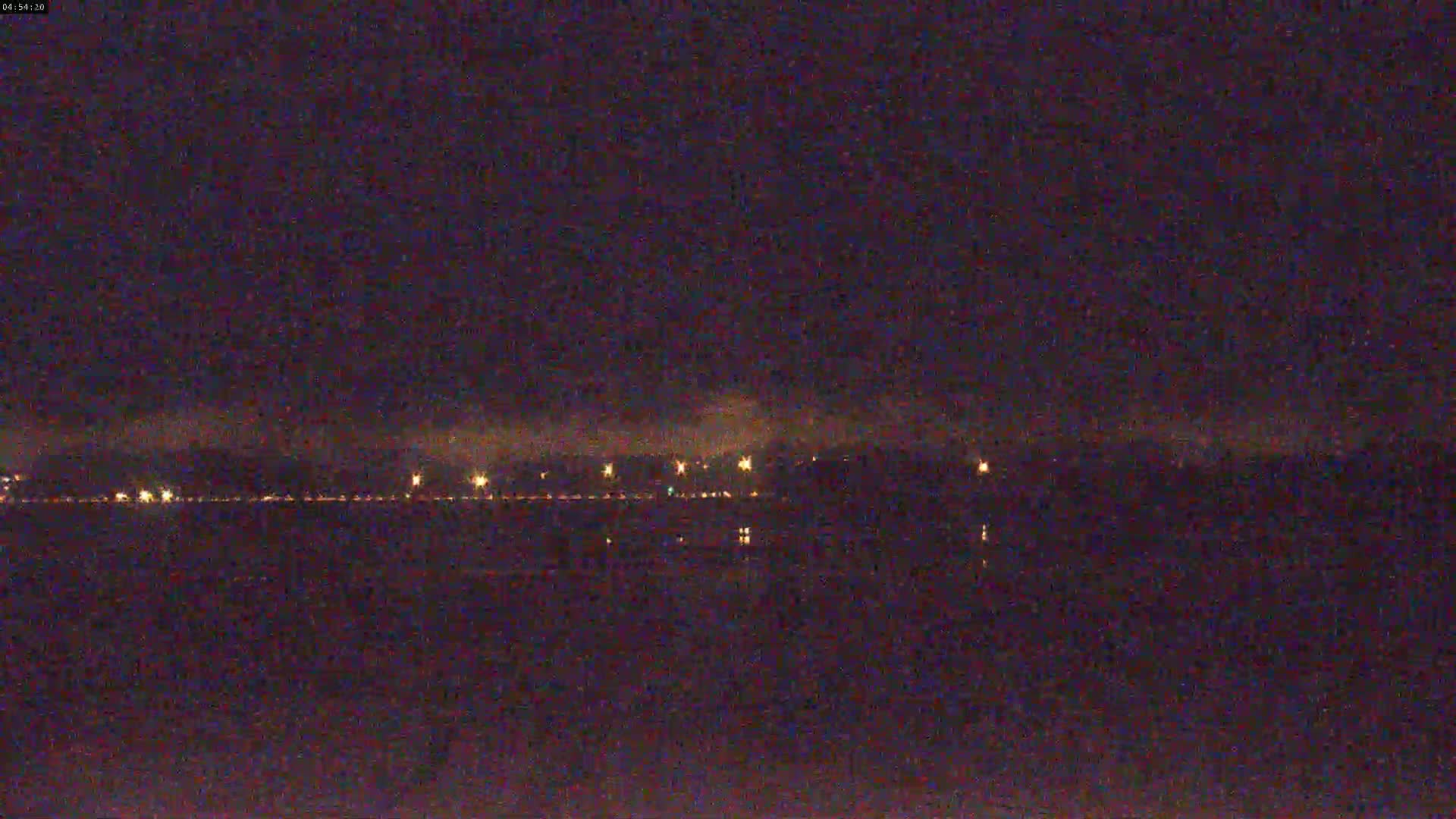 A nighttime view of a body of water with a hazy, faintly lit shoreline in the distance.