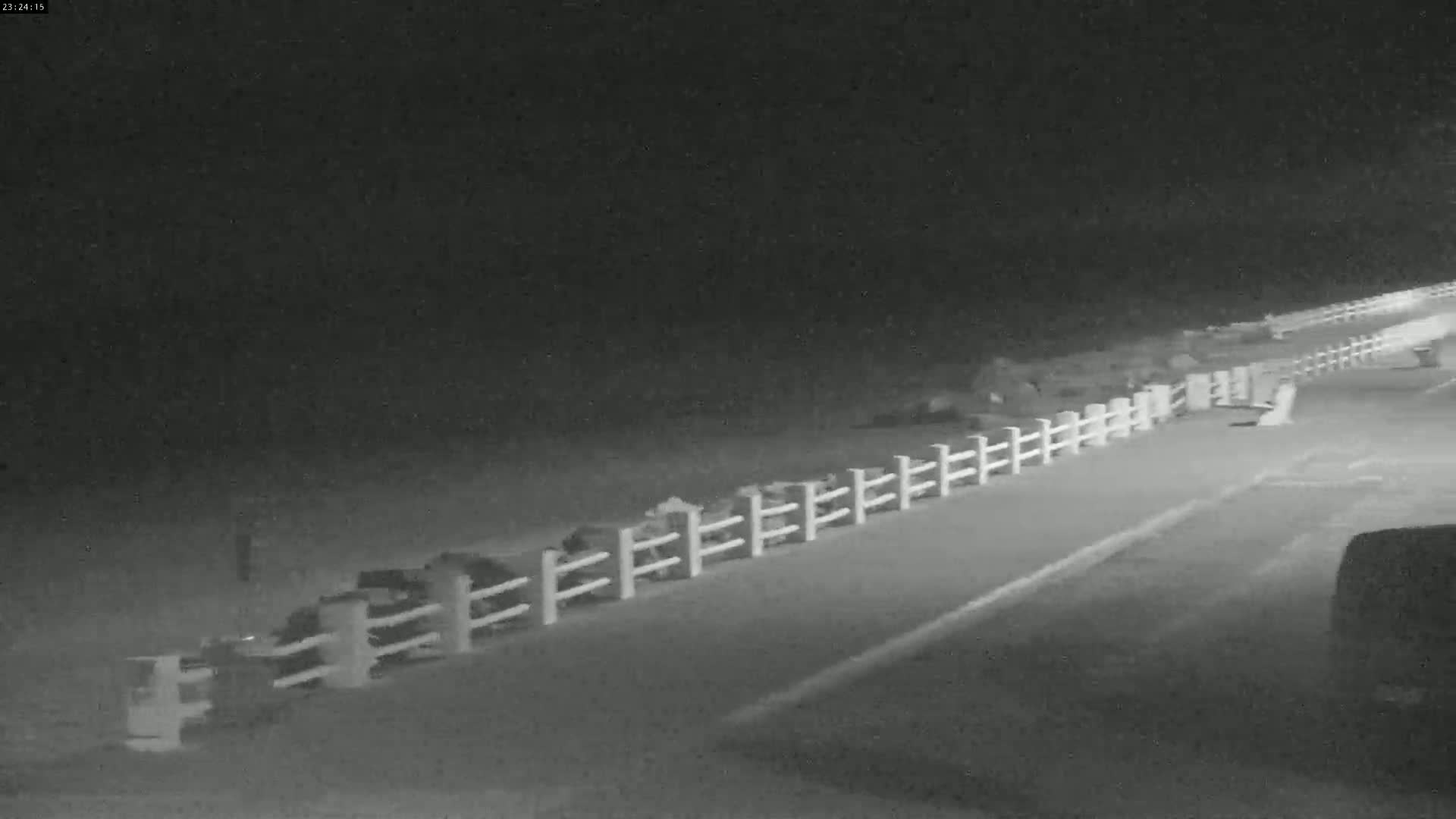 A long, white fence runs alongside a dark road at night.