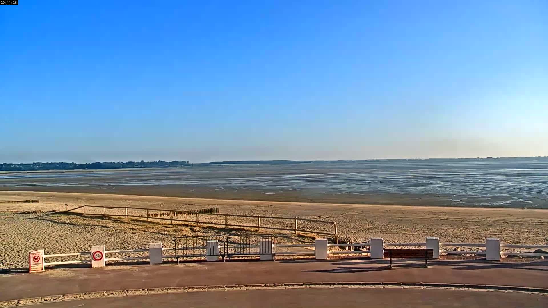 A sandy beach stretches out to a wide expanse of tidal flats under a clear blue sky.