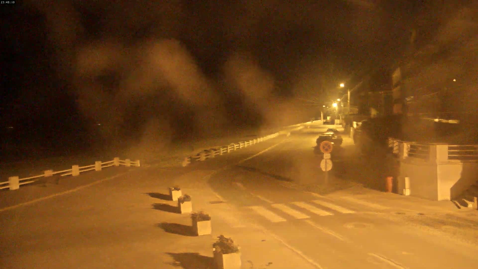 A nighttime street scene shows a road curving to the left, illuminated by streetlights under hazy conditions.