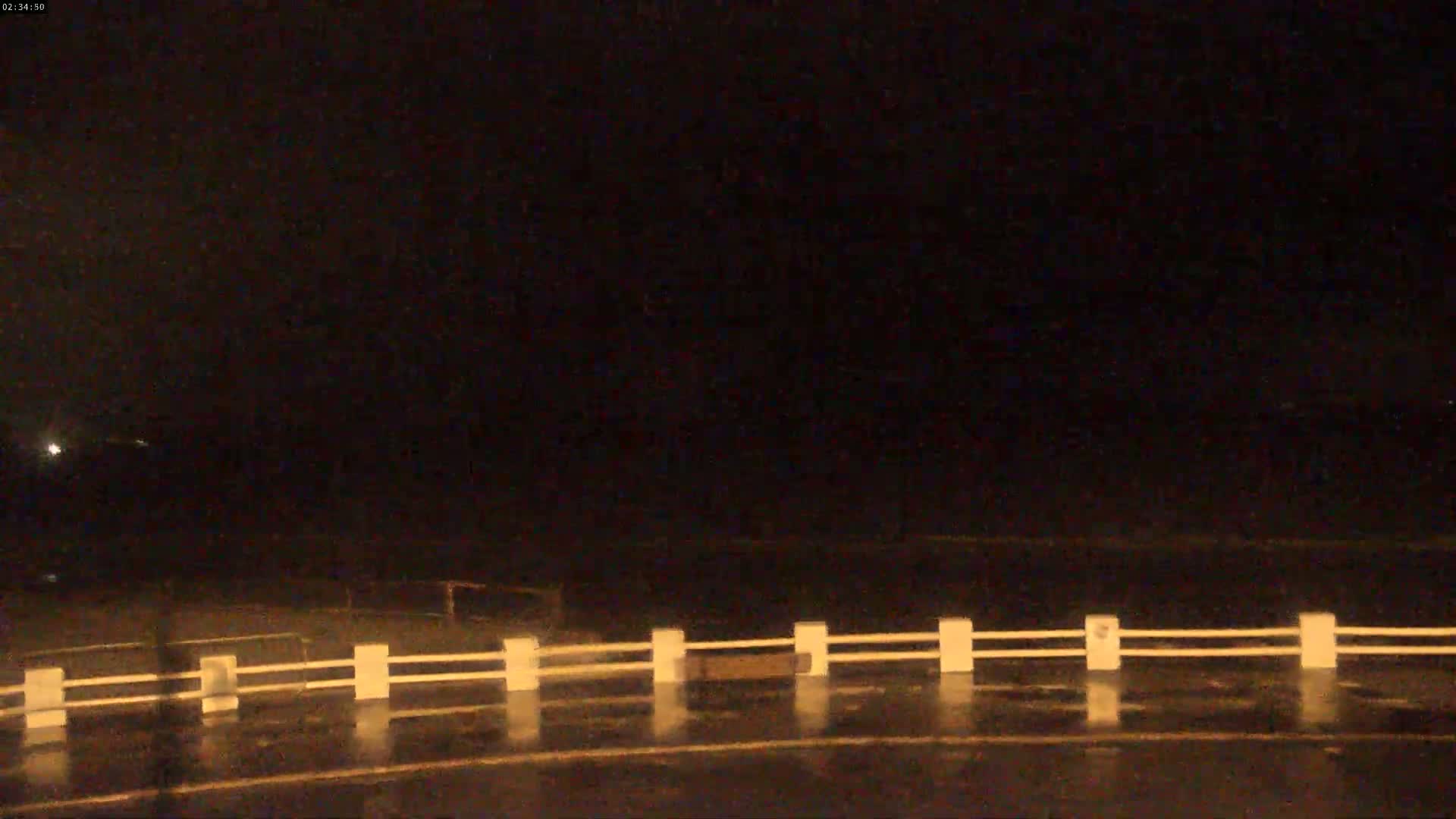 A wet, dark road at night is visible beyond a low white fence.