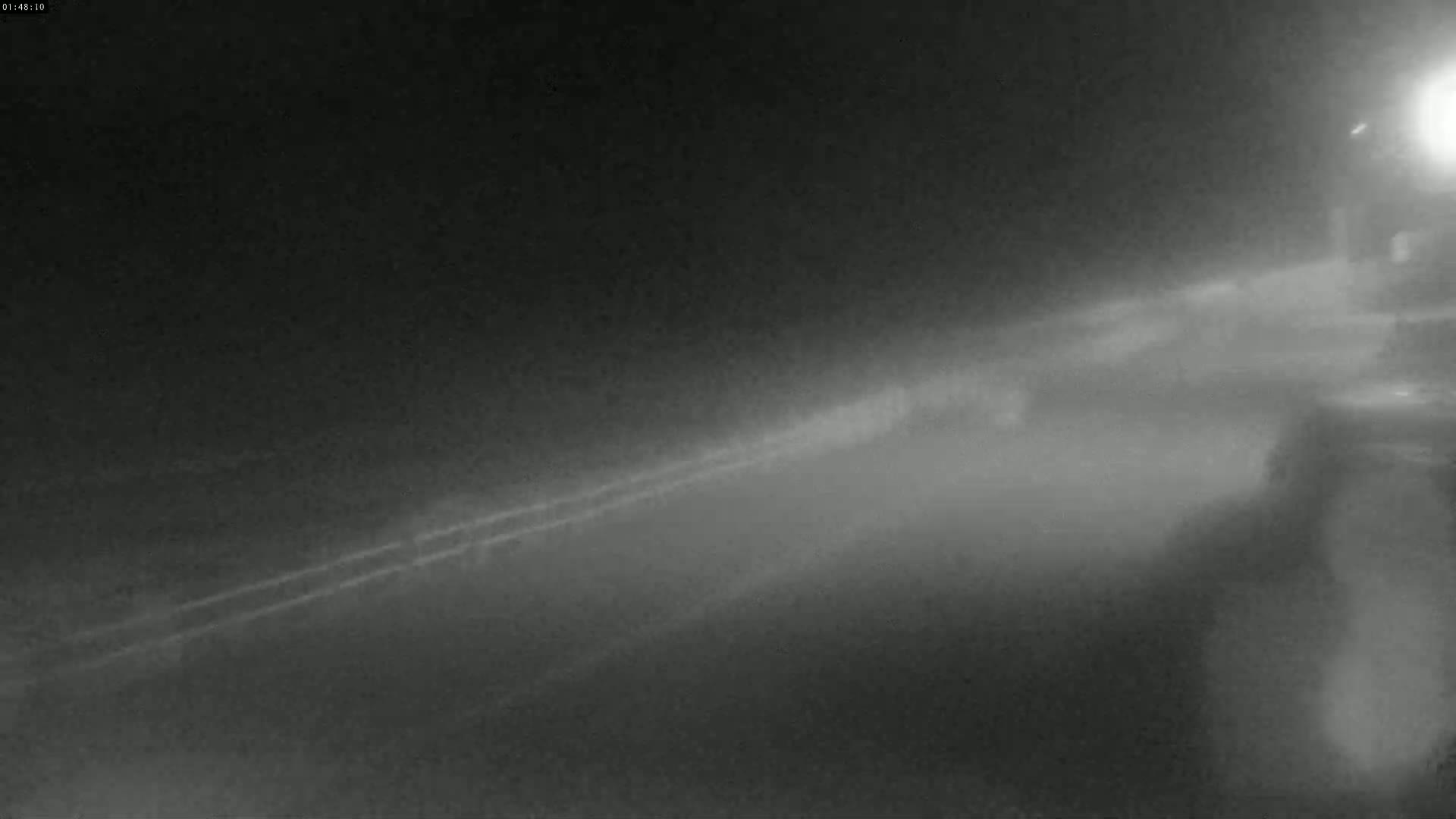 A foggy, nighttime road is seen from a low vantage point, with a barrier and faint lights in the distance.