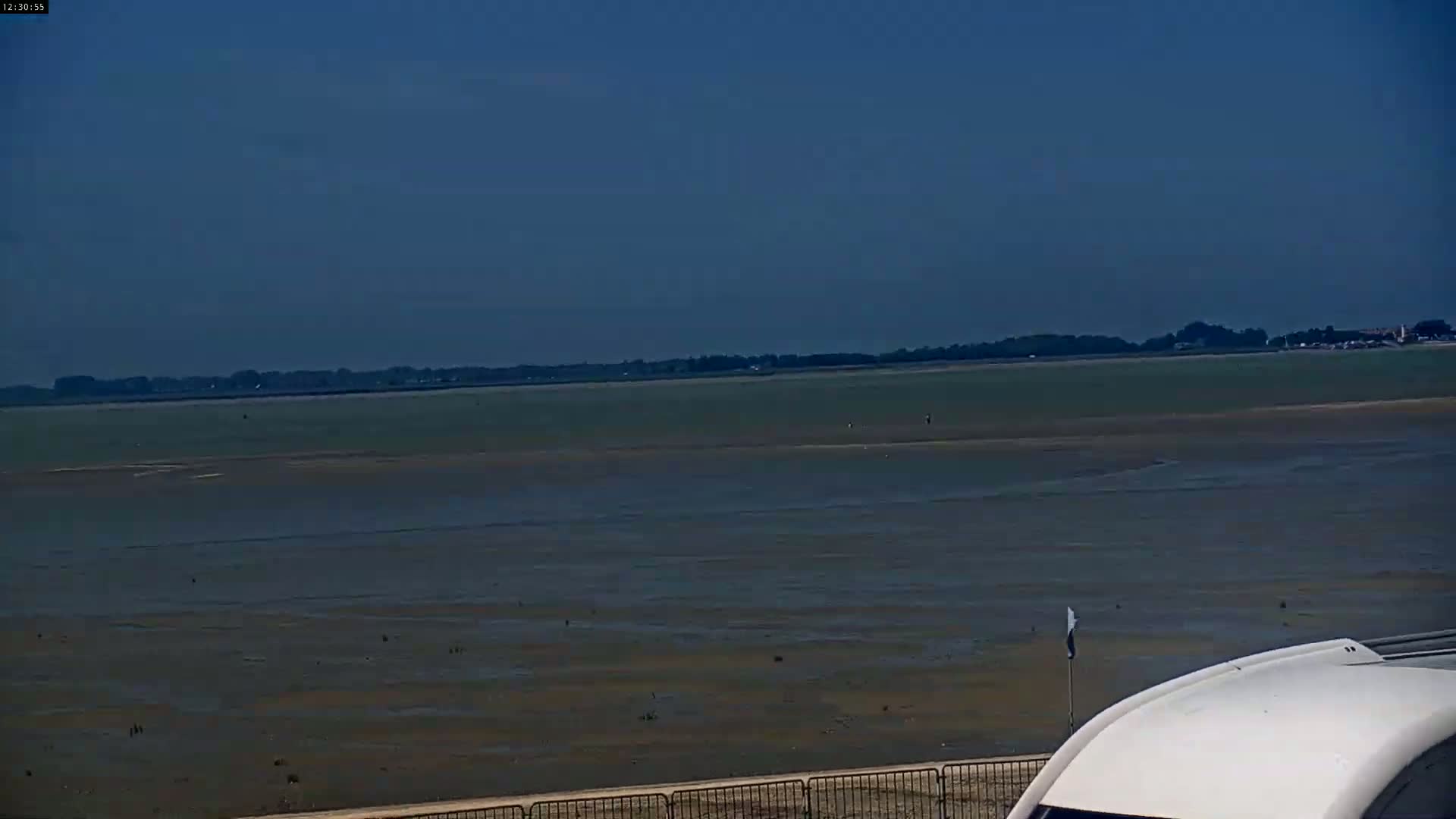 A mostly clear sky overlooks a vast expanse of shallow, muddy water receding from a distant shoreline under a clear sky.