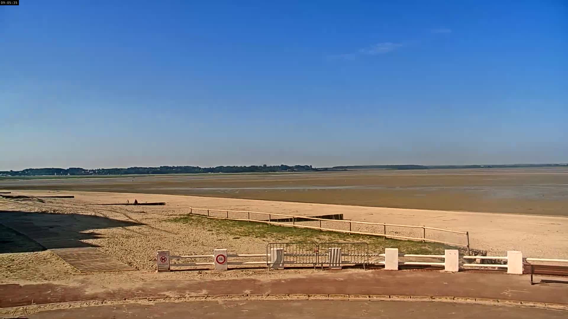 A sandy beach stretches towards a wide expanse of mudflats under a clear blue sky.