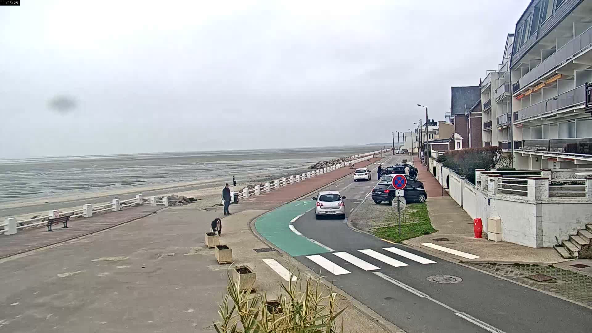 An expansive sandy tidal flat stretches towards a distant coastline under a heavily overcast sky where patches of light indicate the sun attempting to break through.