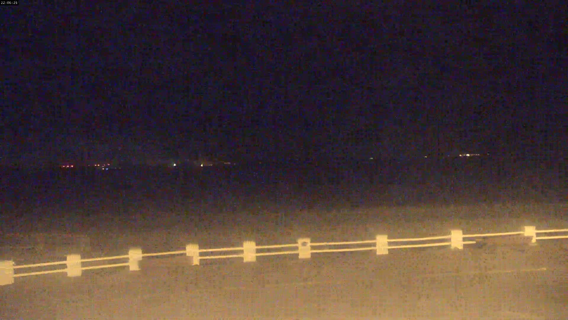 An expansive sandy tidal flat stretches towards a distant coastline under a heavily overcast sky where patches of light indicate the sun attempting to break through.