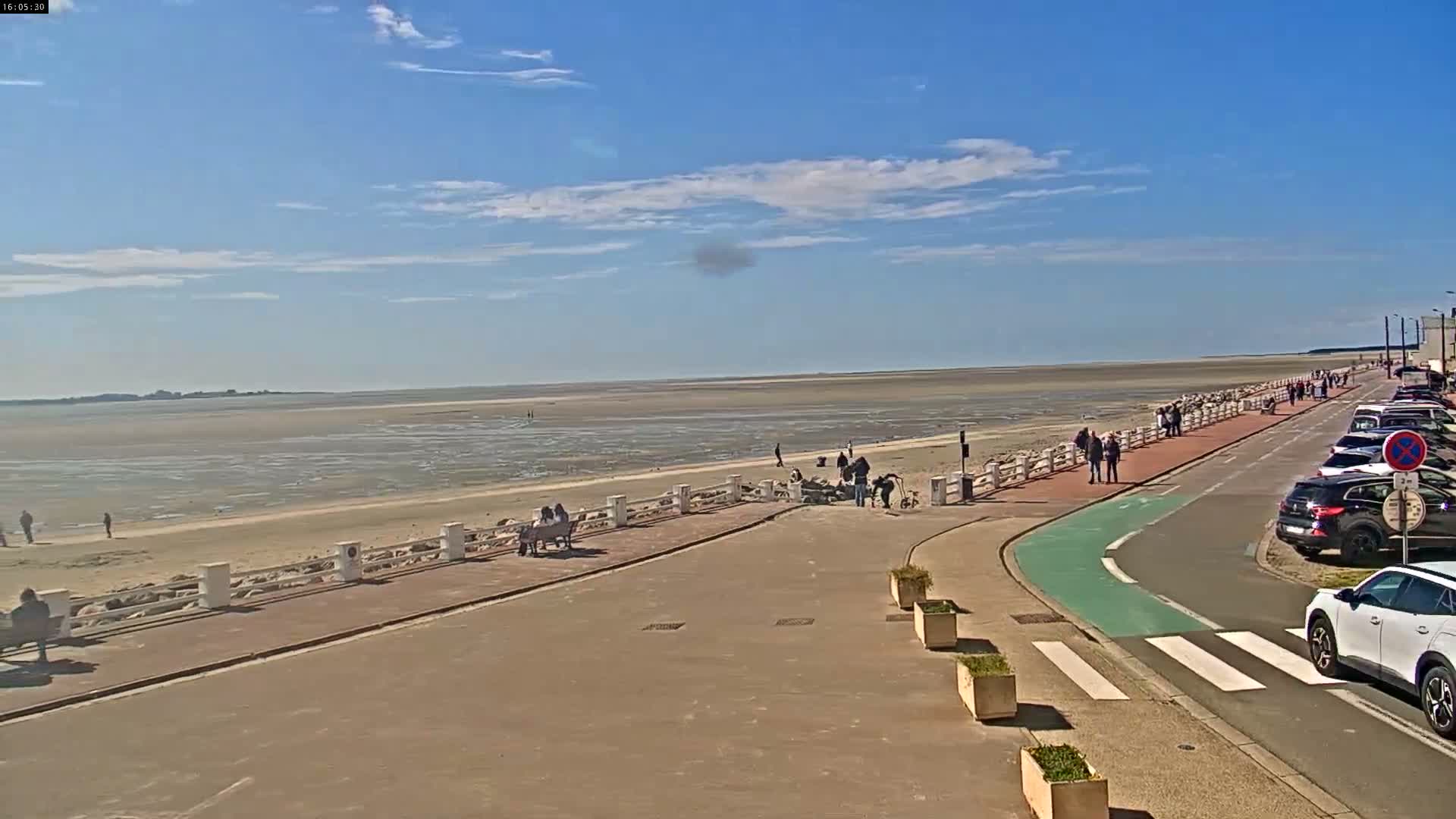 An expansive sandy tidal flat stretches towards a distant coastline under a heavily overcast sky where patches of light indicate the sun attempting to break through.