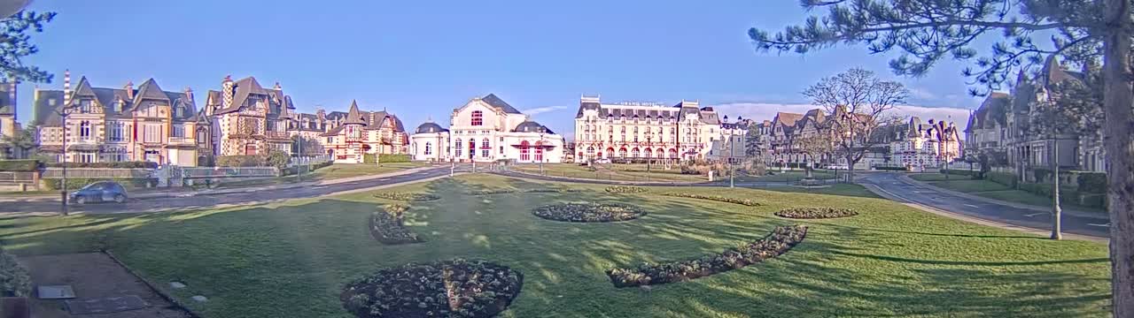 A sunny day reveals a row of elegant European-style buildings across a grassy park with landscaped flower beds.
