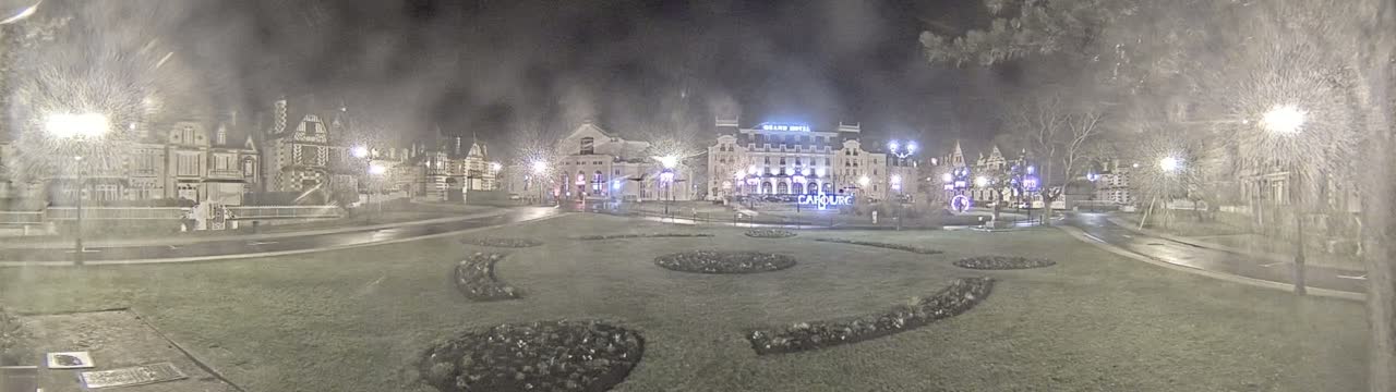 A nighttime view of a town square with several buildings, including a large hotel,  under hazy or snowy conditions.
