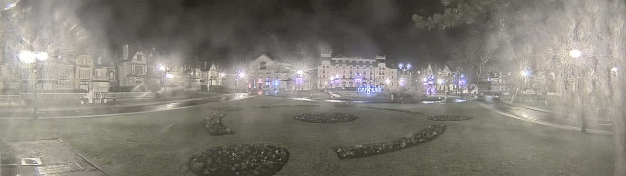 A nighttime scene of a town square with several buildings, including a large hotel, is shown in the midst of a light snow or mist.