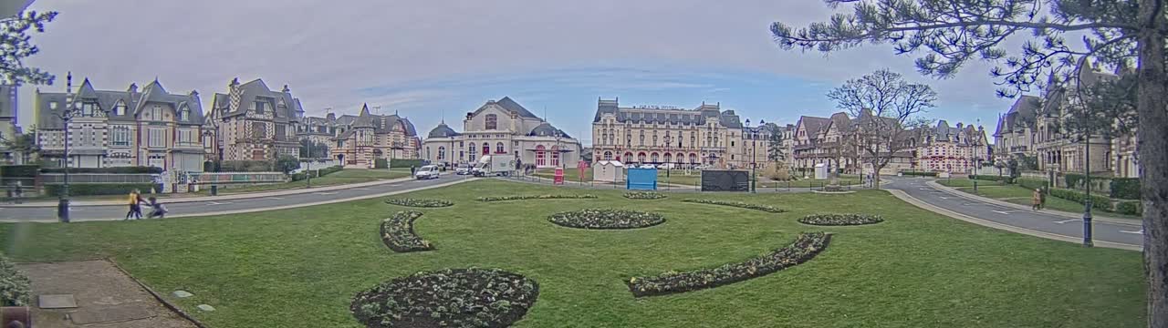 A grassy plaza with landscaped flower beds is situated in front of a row of stately buildings on an overcast day.