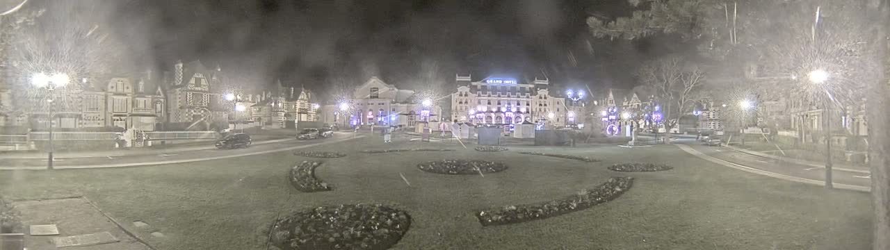 A nighttime scene shows a town square with several buildings, including a large hotel, and landscaped areas, under snowy conditions.