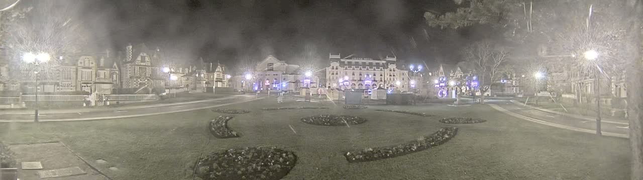 A nighttime view of a town square with several buildings, including a large hotel, surrounded by snow-covered lawns and landscaping.
