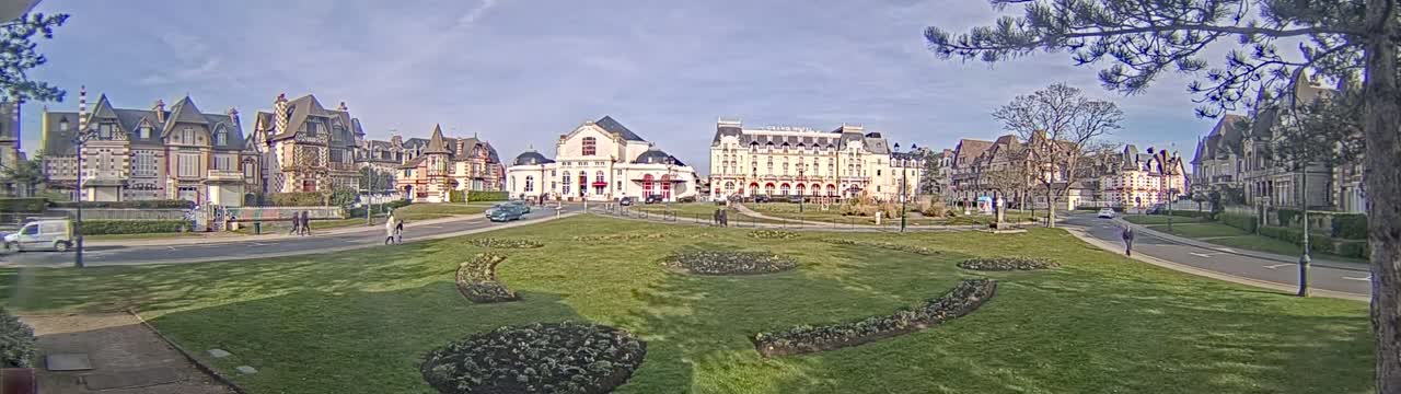 A grassy park with flowerbeds is situated in front of several large, ornate buildings under a mostly clear sky.