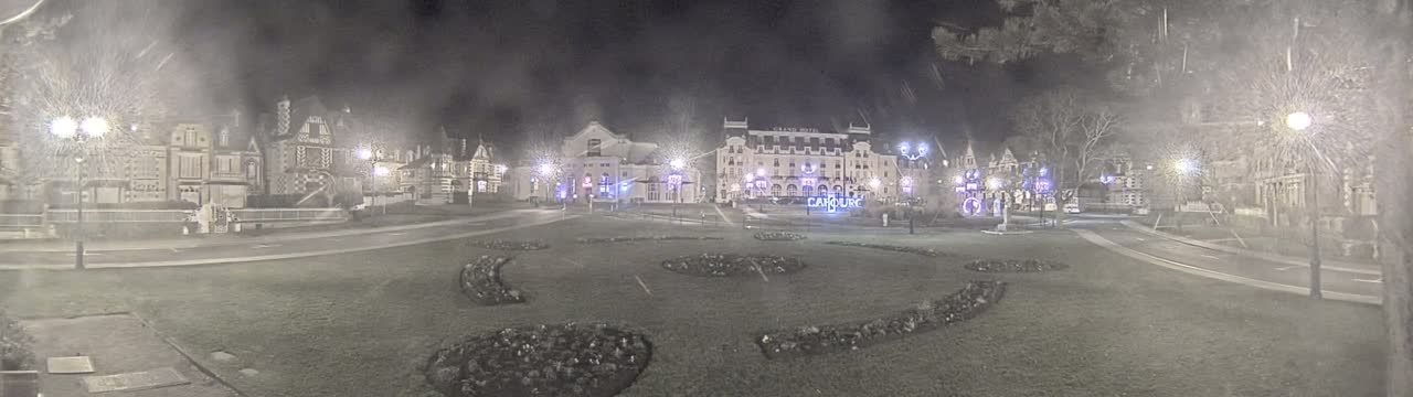 A nighttime view of a town square with several buildings, including a large hotel, lit by streetlights in foggy or snowy conditions.