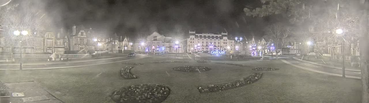 A nighttime view of a town square with several buildings, including a large hotel, under hazy or snowy conditions.