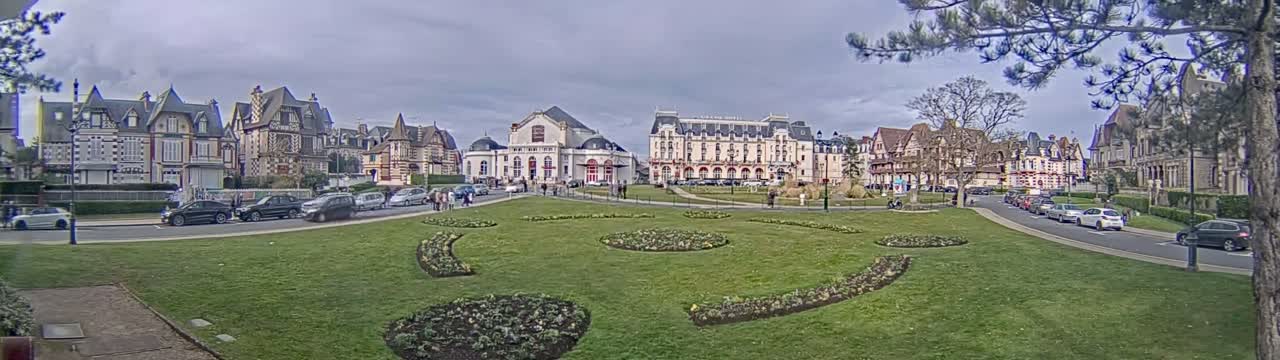 A grassy square with flowerbeds is surrounded by several multi-story buildings under an overcast sky.