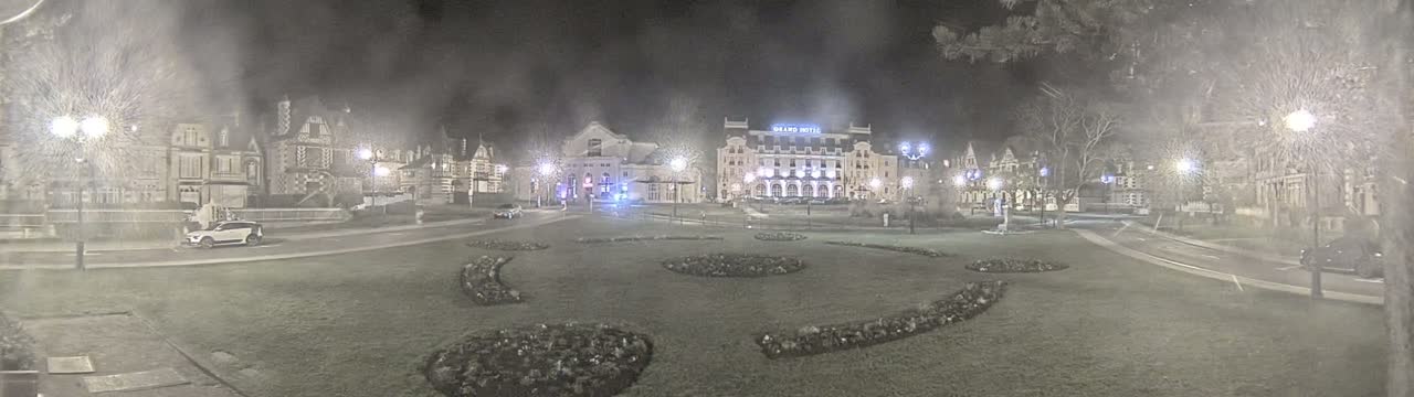 A nighttime view of a town square with several buildings, including a large hotel, illuminated by streetlights in hazy conditions.