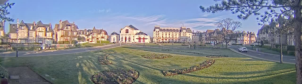 A row of grand, ornate buildings lines a grassy square on a clear, frosty morning.