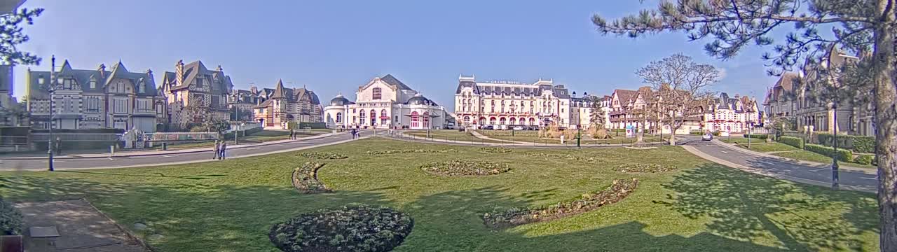A grassy park with manicured flowerbeds is situated in front of a row of stately buildings on a sunny day.
