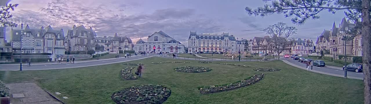 A town square with several large buildings and landscaped gardens under a cloudy, twilight sky.