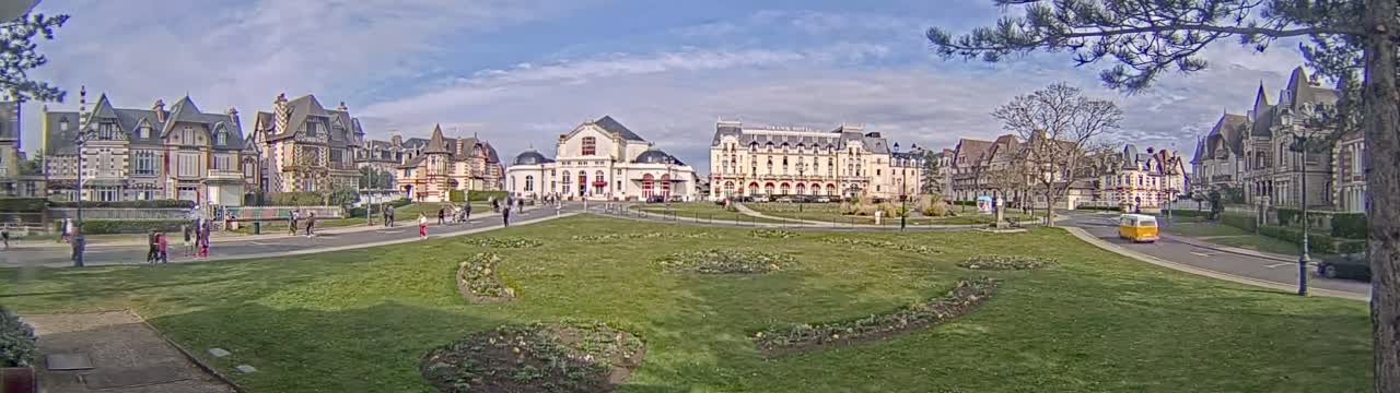 A grassy park separates several large, ornate buildings under a partly cloudy sky.