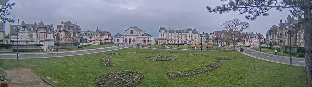 A row of ornate buildings sits across a grassy park, under an overcast sky.